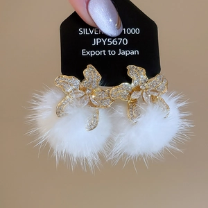 Detail shot of elegant floral earrings with sparkling zircons and fluffy white pom-poms