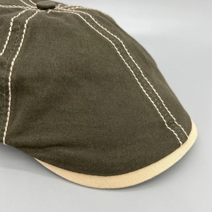 Detail of olive green newsboy cap featuring white contrast stitching and twill cotton fabric