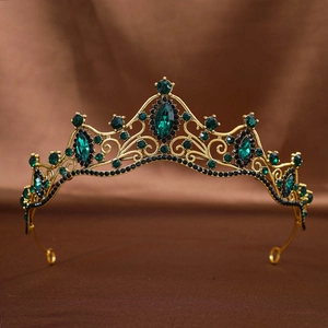 Close-up of vintage gold crown featuring large green gemstones and black rhinestones detailing