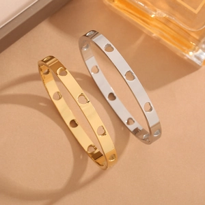Gold and silver stainless steel bangles with hollow heart cutouts on a warm beige background