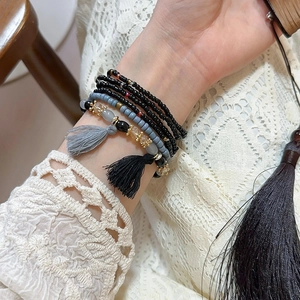 Detail of layered Bohemian beaded bracelet with grey tassels on a lace background