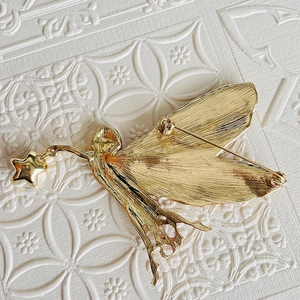 Close-up of a golden fairy brooch with gradient wings and a lucky star pendant charm