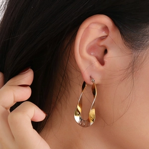 Close-up of a two-tone twisted U-shape hoop earring worn by a model in gold and silver