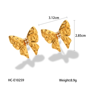 Close-up of golden butterfly drop earrings featuring white crystals and textured details