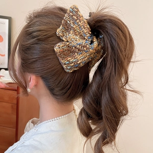 Détail d'une pince à cheveux en tweed multicolore portée sur de longs cheveux bruns