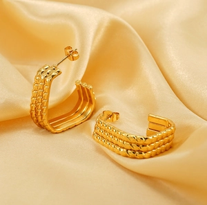 Macro detail of gold-plated U-shaped earrings with unique woven texture on silk fabric