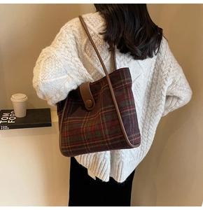 Detail of red and green plaid tote bag with brown leather trim worn by a model