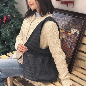 Detail of grey plaid shoulder bag with double pockets worn by a model in a cozy setting