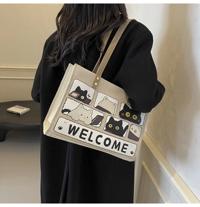 Canvas tote bag with cartoon cat prints and Welcome text shown worn over the shoulder