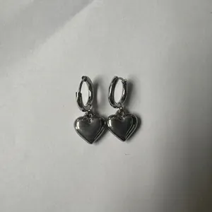 Detailed view of silver stainless steel heart drop hoop earrings on grey background