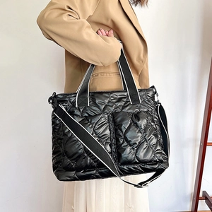 Macro shot of black quilted puffer tote bag with glossy finish and striped handles