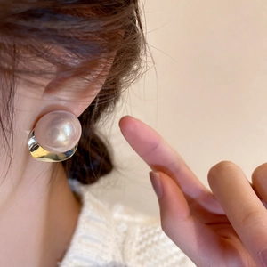 Close-up of a large pink pearl stud earring with golden metal base on a model's ear