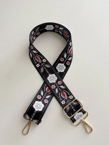Close-up of floral embroidery on wide canvas bag strap with gold metal hooks
