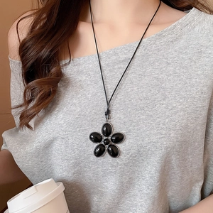 Detail of minimalist black resin flower pendant necklace with silver metal trim on model