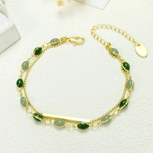 Dettaglio di un bracciale a doppio strato dorato con perline verde smeraldo e barra in metallo