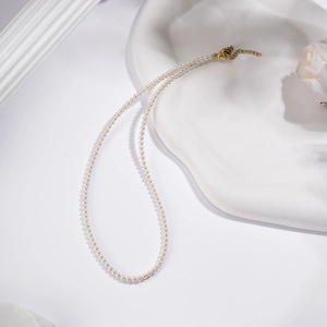 Elegant white pearl necklace with gold lobster clasp on minimalist decorative tray
