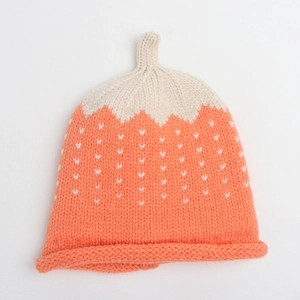 Close-up of strawberry-shaped baby knit hat with orange coral color and white heart patterns
