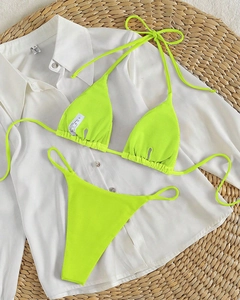 Flat lay of neon green ribbed halter bikini set on a casual white shirt and woven mat