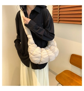 Detail of beige pleated crossbody dumpling bag with soft quilted texture on a wooden chair