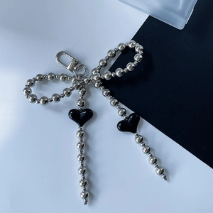 Silver beaded bow keychain with black heart charms on a split black and white background