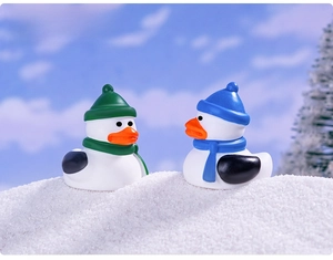 Miniature Christmas duck figurines in winter hats on snowy background for holiday decor