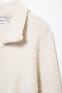 Détail du col en fausse fourrure blanche et de l'étiquette sur le cardigan en maille