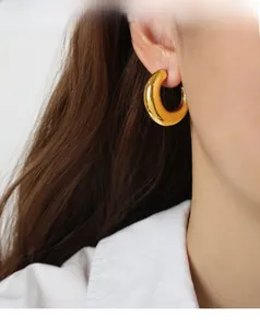 Close-up of polished chunky golden C-shaped hoop earrings worn on a model's ear
