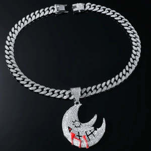 Close-up of iced-out silver moon pendant with red blood teardrops on a Cuban link chain