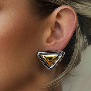 Gros plan d'une boucle d'oreille triangulaire bicolore en acier inoxydable sur le lobe