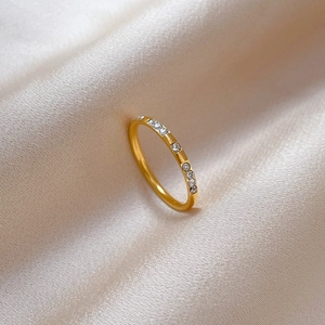 Detail of a thin gold titanium ring with embedded round rhinestones on silk fabric