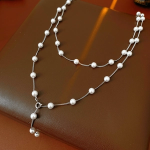 Detail of silver double-layered Y-shaped necklace with white pearls on leather