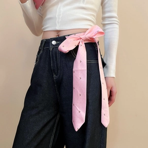 Detail of pink floral silk ribbon belt tied on dark blue denim jeans with a silver buckle