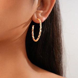 Close-up of golden geometric twisted C-shape earrings on a model with sharp details