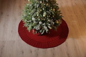 Detailed knit texture of a red Christmas tree skirt around a festive holiday tree base
