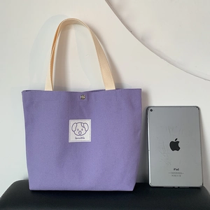 Cute purple canvas tote bag with a cartoon puppy label and cream handles on a white background