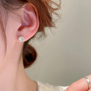 Close-up of minimalist square cat-eye stone earrings and wavy silver ring on a model