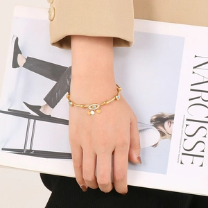 Detail of gold evil eye cuff bracelet with heart charms worn by model with a magazine