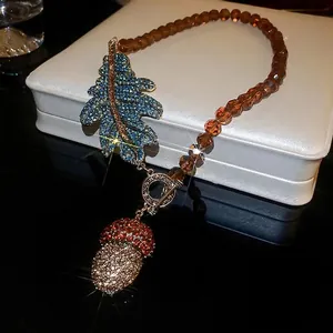 Collier vintage avec pendentif pomme de pin, feuille de strass bleu et perles ambre