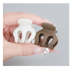 Detailed view of mini matte pumpkin hair claws in white and brown, shown in hand for scale
