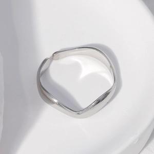 Macro shot of silver wave-shaped adjustable stainless steel ring on a white artistic base