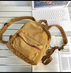 Detailansicht eines senfgelben Canvas-Rucksacks auf Schreibtisch neben Laptop und Magazin