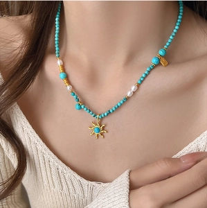 Détail du collier avec perles de turquoise et pendentif soleil doré sur le cou