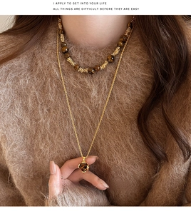 Dettaglio della collana a strati in oro con perle occhio di tigre su un maglione