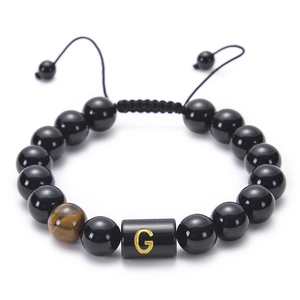 Close-up of black onyx bead bracelet featuring a golden letter G and tiger eye stone