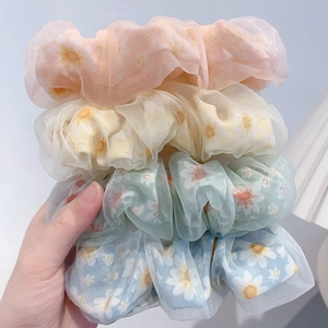 Close-up of four organza daisy hair scrunchies in pink beige green and blue colors