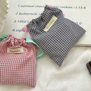 Detail of gingham drawstring bags with embroidered labels in red and black patterns