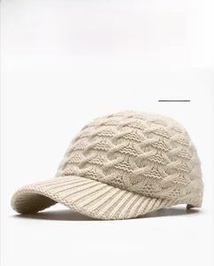 Close-up of beige knitted baseball cap featuring a thick cable knit texture and curved brim