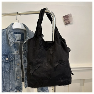 Detail of black lace tote bag featuring 3D butterfly appliques hanging on a hanger