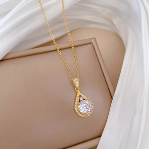Close-up of gold teardrop pendant with central stone on beige jewelry box and silk