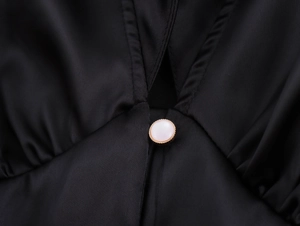Detail of a black satin dress featuring a golden pearl button and delicate pleated fabric